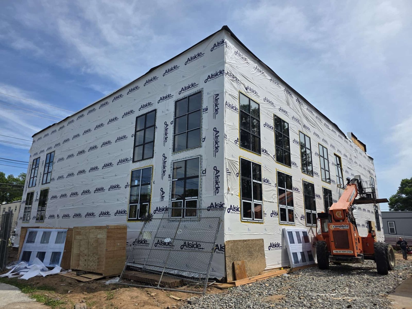 Three-story building at house-wrap stage with black-framed grid windows installed throughout