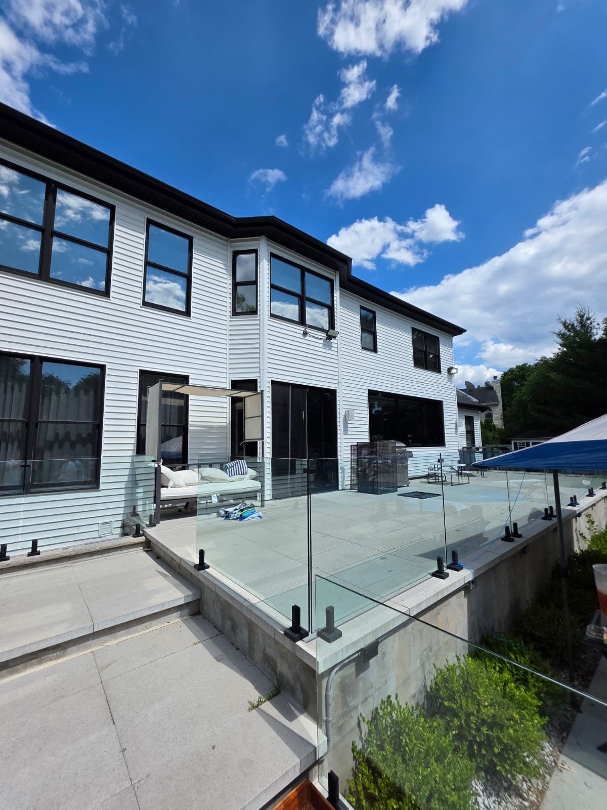 Finished white-clad home rear elevation with black-framed windows, black sliding doors, and a frameless glass deck railing