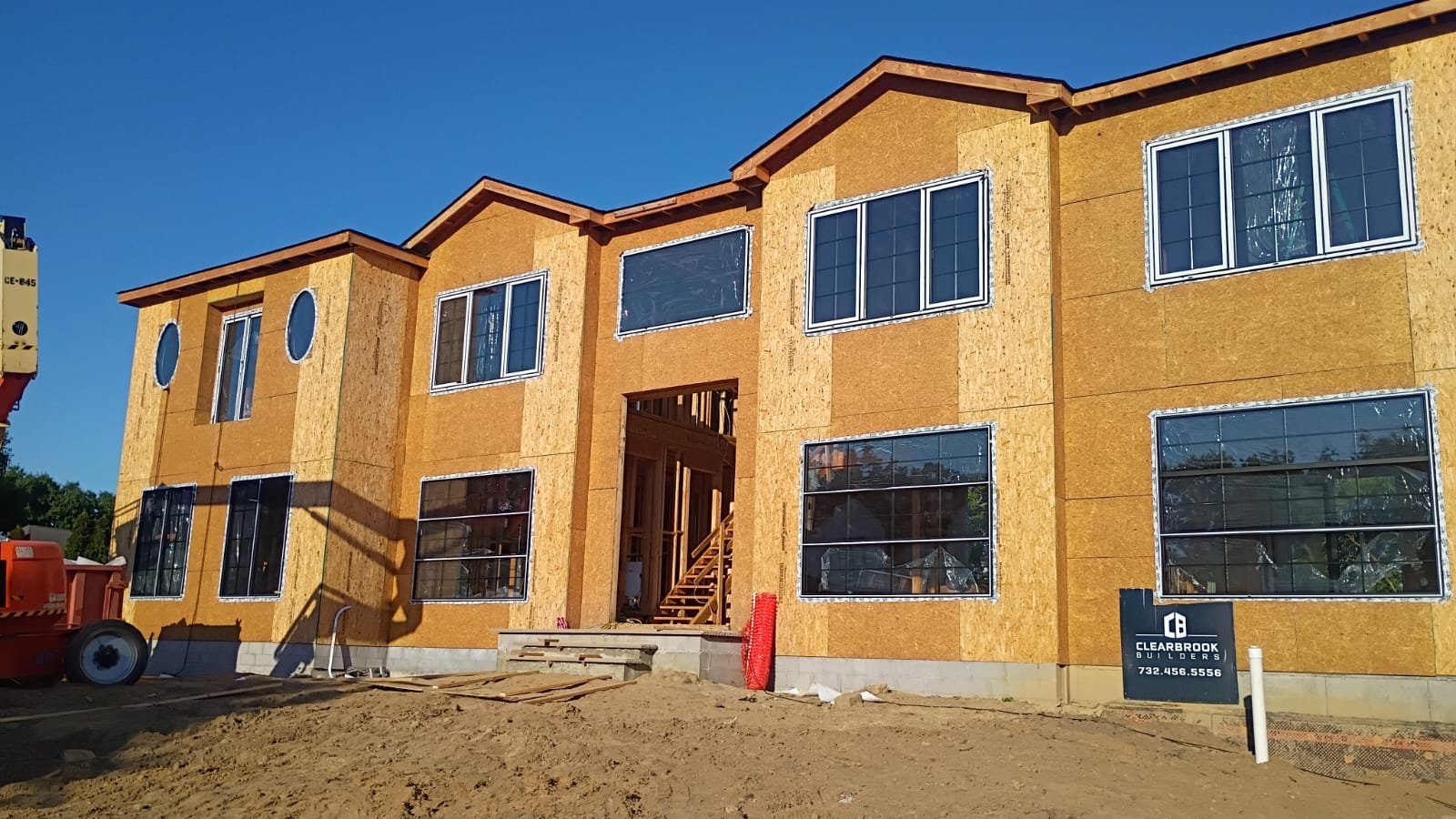 Front elevation of a large home at sheathing stage with grid windows, picture windows, and round accent windows set in place